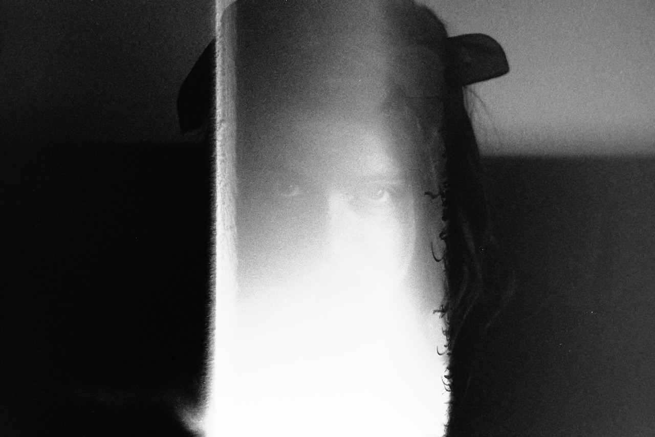 A black and white portrait picture of a female face looking at the camera, only her eyes and hair are visible. The bottom-middle of picture seems to be torn or underdeveloped, her eyes are looking directly at the lens of the camera.